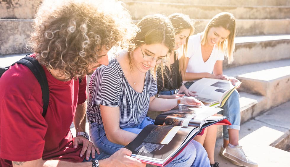 Group of diverse students studying together outdoors with books.