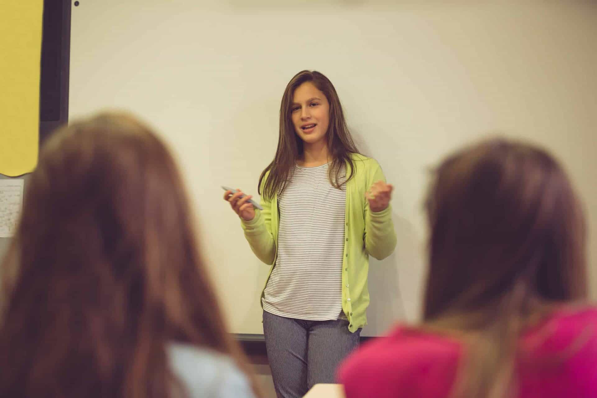 Young woman giving a presentation to students in a classroom setting.