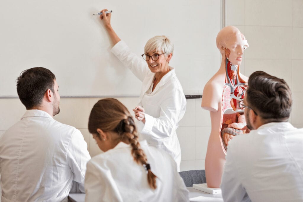 Medical students learning with a teacher and anatomical model in classroom.
